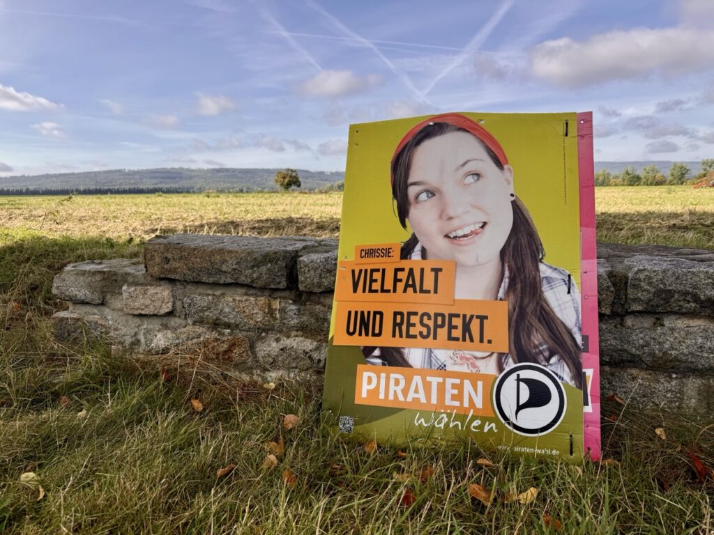 Plakat steht an einer niedrigen Natursteinmauer, im Hintergrund Felder und der Wald Deister. Plakattext: Vielfalt und Respekt. Piraten wählen.
